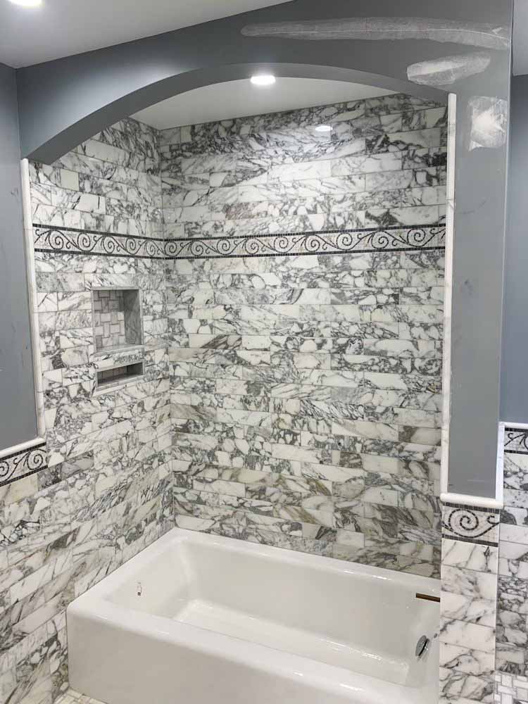 Marble looking ceramic tile wall with Victorian stencil pattern accent, a bathtub, and a basketweave tile bath niche