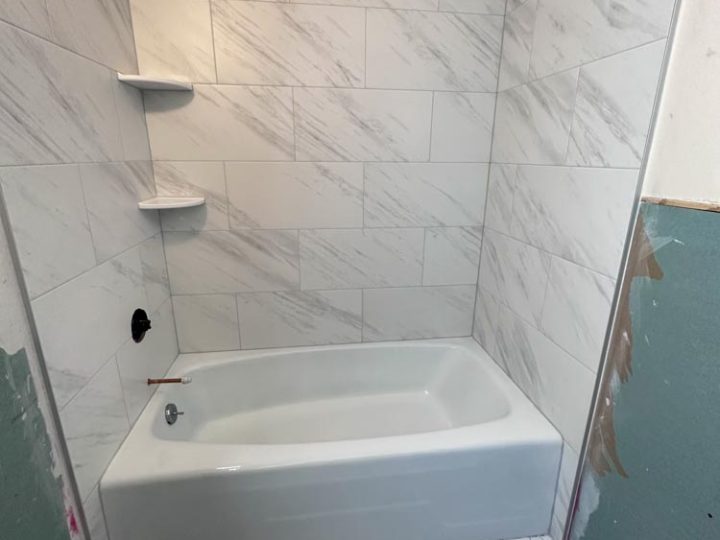Mosaic tile flooring and a ceramic tiled wall surrounding the tub area with corner shower shelves