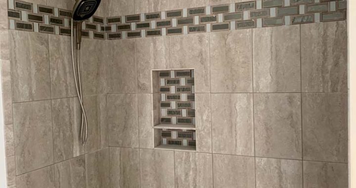 Marble tiled shower wall accentuated with dark-colored tile border and shower niche