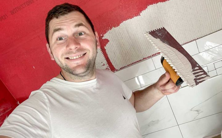 Tile contractor holding a square-notch trowel with adhesive for tile wall installation