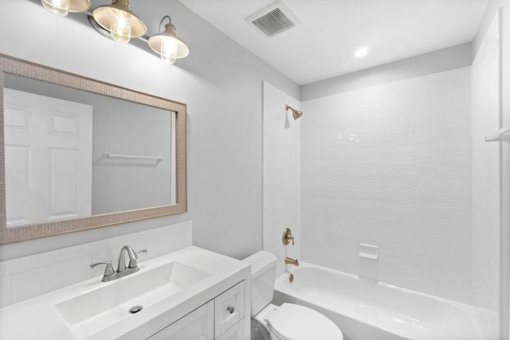 Plain white bathroom with bronze fixtures and a metal vintage-inspired vanity light